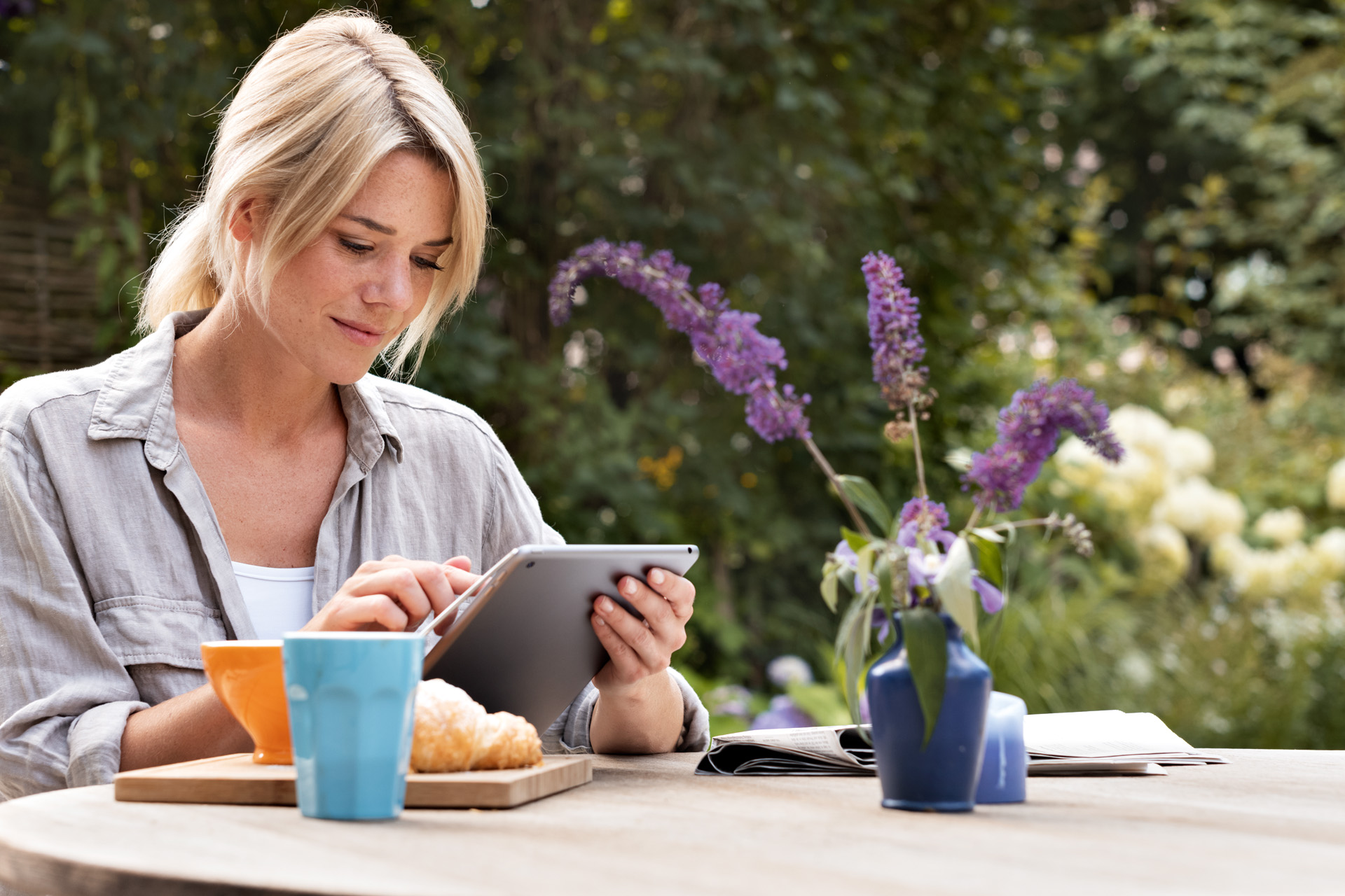 En kvinde, der bruger en tablet ved et morgenbord i en have